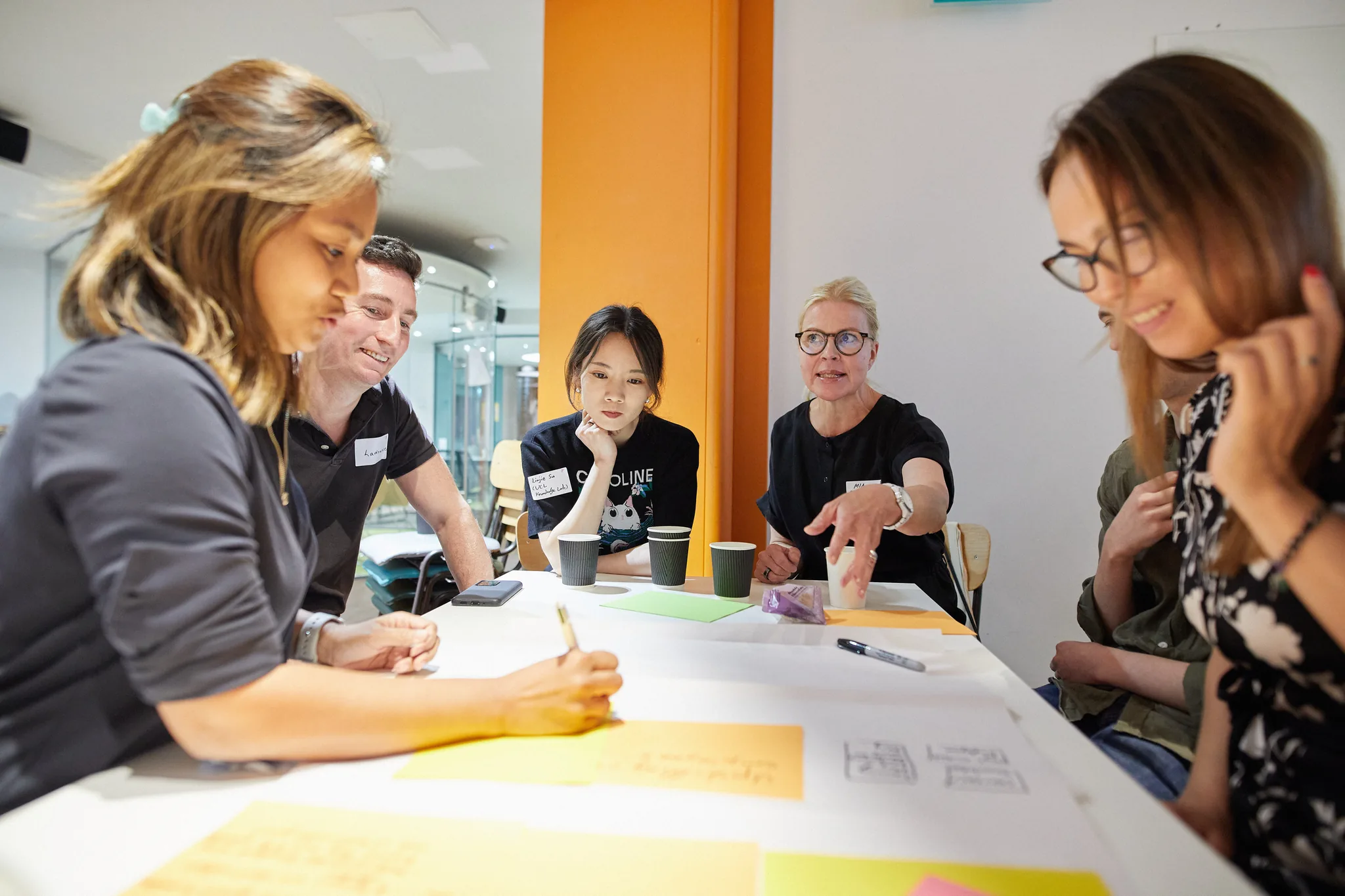 A cohort leaning over a shared canvas on a table, annotating it together